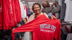 Lady smiling holding a Montclair State University long sleeve shirt at the book store.
